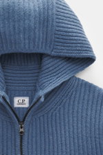 Nahaufnahme der Kapuze einer graublauen C.P. Company Strickjacke, Strick aus Schurwolle und Microfaser, weiche Qualität, voluminöses Strickbild sichtbar.