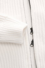 Nahaufnahme der C.P. Company Strickjacke offwhite von schräg oben mit voluminösem Strickbild, Slim Fit, robuster Zwei-Wege-Reißverschluss, gestrickter Kapuze, schrägen Eingriffstaschen, Zipper-Tasche am Oberarm, labeltypischem Linsen-Detail, Strick aus Sc