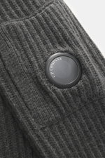 Nahaufnahme der labeltypischen Linse an der gestrickten Kapuze der C.P. Company Strickjacke dunkelgrau mit voluminösem Strickbild, weicher Qualität, Slim Fit, robustem Zwei-Wege-Reißverschluss, schrägen Eingriffstaschen und Zipper-Tasche am Oberarm, Stric