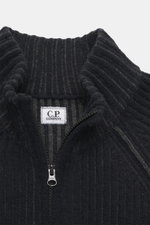 Nahaufnahme von C.P. Company Strickjacke navy/dunkelgrau, fotografiert von oben, mit Stehkragen, voluminösem Strickbild, robustem Zwei-Wege-Reißverschluss, Zipper-Tasche am Oberarm, Raglanärmeln, Regular Fit, labeltypischem Linsen-Detail, weicher Qualität