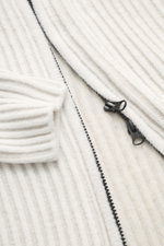 Nahaufnahme der C.P. Company Strickjacke offwhite mit voluminösem Strickbild, robustem Zwei-Wege-Reißverschluss, Raglanärmel, Stehkragen, Zipper-Tasche am Oberarm, aus weichem Schurwolle-Microfaser-Mix, Regular Fit, perspektivisch frontal fotografiert.