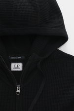 Nahaufnahme der Kapuze und des robusten Reißverschlusses der C.P. Company Strickjacke 'Metropolis' schwarz, Regular Fit, weicher Griff, Mix aus Schurwolle und Microfaser, Kapuze mit Tunnelzug, Tasche am Arm mit Logo-Patch, flexible Rippbündchen.
