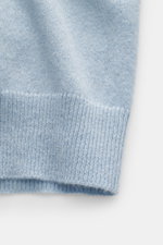 Nahaufnahme der hellblau melierten FTC Cashmere Strickjacke, Detailansicht des feinen Strickbilds und geripptem Saum aus Fair-Trade-Cashmere, weich und nachhaltig produziert.