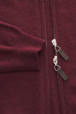 Nahaufnahme der bordeauxfarbenen FTC Cashmere Strickjacke bordeaux von oben auf Ärmel und verdeckten Zwei-Wege-Reißverschluss mit Leder-Logo, feines Strickbild, gerippter Stehkragen, flexible Bündchen, Fair-Trade-Cashmere, OEKO-TEX® zertifiziert.