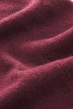 Nahaufnahme des feinen Strickbilds und weichen Griffs der FTC Cashmere Strickjacke bordeaux aus Fair-Trade-Cashmere, Perspektive schräg von oben.