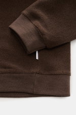 Close-up front view of the cuff and hem of the 04651/ A trip in a bag Rundhalspullover dunkelbraun, a soft fleece pullover made from a wool-cotton blend with ribbed cuffs and hem, featuring a white side seam web label.

Description: <p>Legeres Layering Pi