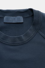 Close-up front view of Stone Island Sweatshirt 'Ghost Piece' graublau neckline showing soft, slightly elastic cotton fabric with tonal compass badge on sleeve, raglan sleeves, round neck, regular fit, and comfortable cuffs for casual wear. <p>STONE ISLAND
