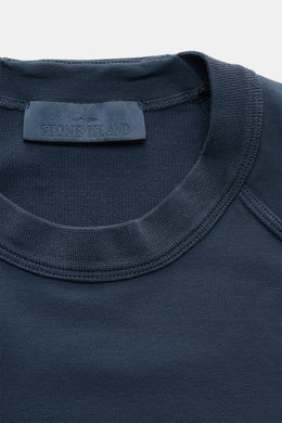 Close-up front view of Stone Island Sweatshirt 'Ghost Piece' graublau neckline showing soft, slightly elastic cotton fabric with tonal compass badge on sleeve, raglan sleeves, round neck, regular fit, and comfortable cuffs for casual wear. <p>STONE ISLAND