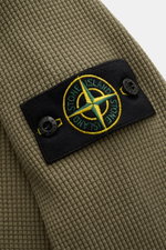 Close-up side view of the Stone Island Rundhalspullover 'Waffle' oliv showing olive waffle-knit cotton fabric and black compass badge on the upper arm. Basic Piece mit Twist: Dieser Pullover im Waffelstrick von STONE ISLAND wird zur idealen Grundlage mode