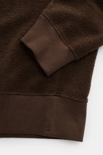 Nahaufnahme des Stone Island Frottee-Rundhals-Sweatshirts dunkelbraun, detailreich von unten rechts fotografiert, zeigt Raglanärmel, breite Rippbündchen und die schwere Baumwolle-Microfaser-Qualität.