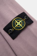 Nahaufnahme des Stone Island Longsleeve mauve aus schwerem Baumwolljersey mit Kompass-Badge auf dem Ärmel, fotografiert von schräg oben.