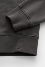 Nahaufnahme des Stone Island Rundhals-Sweatshirts "Basic Sweat" dunkelgrau von unten mit Fokus auf Rippbündchen, weichem Baumwollstoff und Kompass-Badge am Oberarm. Zeitloses Basic Piece, Regular Fit, Rundhalsausschnitt, komfortable Bündchen.