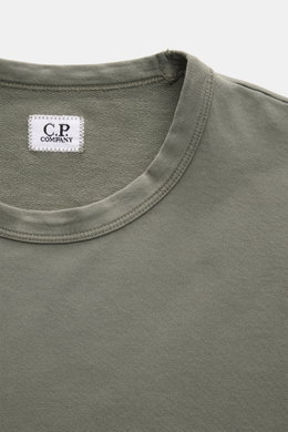 Close-up front top view of a C.P. Company Sweatshirt salbei in a slim fit, garment-dyed light olive green cotton with a round neckline and visible white label, showcasing soft fabric texture and neat stitching. <article class="text-token-text-primary w-fu
