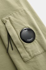 Close-up perspective of the sleeve of the C.P. Company Sweatshirt oliv, showing the olive garment-dyed cotton fabric, slim fit, round neckline, and the signature lens detail on the black zipper pocket at the upper arm with flexible ribbed cuffs. <article 