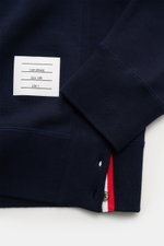 Nahaufnahme des navyfarbenen Thom Browne Rundhals-Sweatshirts aus reiner Baumwolle mit Rippbündchen, grosgrain-Schlaufe rückseitig und geknöpften Saumschlitzen, fotografiert aus seitlicher Perspektive.