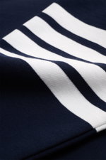 Nahaufnahme des navyfarbenen Thom Browne Rundhals-Sweatshirts mit weißen Kontraststreifen am Ärmel, weiche Baumwolle, Grosgrain-Schlaufe rückseitig, aus schräger Perspektive.