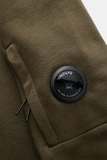Nahaufnahme des olivfarbenen C.P. Company Sweatshirts, seitliche Perspektive auf die Ärmeltasche mit labeltypischem Linsen-Detail aus reiner Baumwolle.