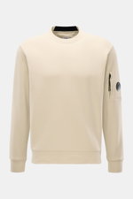 C.P. Company Sweatshirt sand aus reiner Baumwolle, leichte Qualität, Rundhalsausschnitt, Front- und Ärmelansicht mit labeltypischem Linsen-Detail an Ärmeltasche.