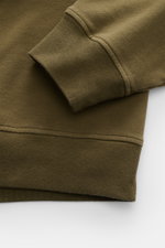 Nahaufnahme des Stone Island Sweatshirts 'Ghost Piece' oliv von schräg oben, Fokus auf elastische Rippbündchen und weiche Baumwollqualität.