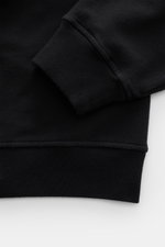 Nahaufnahme des Stone Island Sweatshirt 'Ghost Piece' schwarz, zeigt elastische Baumwollqualität, Rippbündchen, Regular Fit, tonales Kompass-Badge am Ärmel.