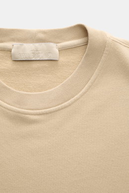 Nahaufnahme des Rundhalsausschnitts vom Stone Island Sweatshirt 'Ghost Piece' beige, fotografiert von oben, mit weichem, elastischem Baumwollstoff und Rippbündchen.