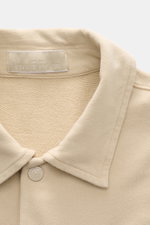 Nahaufnahme des beigen Stone Island Longsleeve Sweat-Poloshirts 'Ghost Piece' aus weichem Baumwollsweat mit Polokragen und STONE ISLAND-Patch, frontal fotografiert.