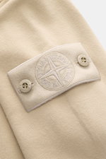 Nahaufnahme des Stone Island Longsleeve Sweat-Poloshirt 'Ghost Piece' beige mit weichem Baumwollsweat und STONE ISLAND-Patch am Oberarm, von schräg oben fotografiert.