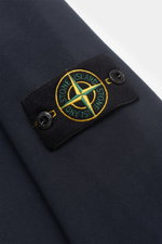 Close-up view of the Stone Island Rundhals-Sweatshirt 'Basic Sweat' navy sleeve, showcasing the black compass badge with yellow and green embroidery and branded buttons on navy cotton fabric.

<p>Zeitloses Basic Piece: Das sportive Sweatshirt von STONE IS