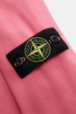 Close-up angled view of the compass badge on the upper arm of the Stone Island Crewneck Sweatshirt 'Basic Sweat' magenta, made of pure cotton with a soft touch, regular fit, crew neckline, and ribbed cuffs.