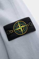 Close-up of the Stone Island R-Neck Longsleeve smoky blue showing the ribbed knit fabric and the compass badge from a side angle.

<p>Autumn essential: The long sleeve by STONE ISLAND combines characteristic ribbed knit structure with timeless versatility