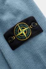 Close-up of the Stone Island Corduroy Sweatshirt Smoky Blue fabric and compass badge, photographed from a top angle.

Description: <p>This sweatshirt from STONE ISLAND is made from pure cotton corduroy, giving it a special twist – perfect to combine with 