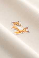 Nahaufnahme des Maison Kitsuné Sweatshirt beige mit weichem Baumwollstoff und typischem Fuchs-Patch auf der Brust, Detail von schräger Perspektive.