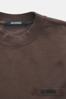 Nahaufnahme des Jacquemus Sweatshirts 'Gros Grain' dunkelbraun, von oben fotografiert, Sweat aus reiner Baumwolle, schwere Qualität, soft, Overlock-Nähte, Regular Fit, Rundhals, Grosgrain mit Logo-Stitching, Rippbündchen.