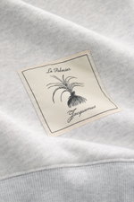 Nahaufnahme des Jacquemus Sweatshirts 'Torneo' hellgrau meliert von oben, zeigt Patch am Saum, Sweat aus reiner Baumwolle, soft, Regular Fit, Rundhals, Logo-Stitching, Rippbündchen.