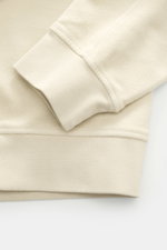 Nahaufnahme des Ärmelbündchens vom C.P. Company Sweat-Troyer sand, fotografiert von oben, Sweat aus reiner Baumwolle, weicher Griff, Regular Fit, Troyer-Kragen mit Reißverschluss, aufgesetzte Tasche am Oberarm, labeltypisches Linsen-Detail, flexible Rippb