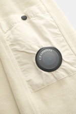 Nahaufnahme aus schräger Perspektive des C.P. Company Sweat-Troyer sand mit weichem Griff, Regular Fit, Troyer-Kragen, Oberarmtasche, Linsen-Detail und Rippbündchen.