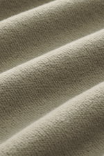 Nahaufnahme des Stoffes eines salbeifarbenen C.P. Company Sweatshirts, weich, reine Baumwolle, Inside-Out-Design, mit Linsen-Detail am Oberarm, fotografiert in Detailperspektive.