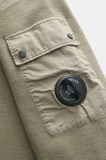 Nahaufnahme des C.P. Company Sweatshirts salbei im Inside-Out-Design, zeigt Ärmel mit praktischer Tasche, Linsen-Detail und weichem Baumwollstoff.