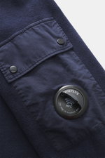 Nahaufnahme aus schräger Perspektive des navyfarbenen C.P. Company Sweatshirts mit Inside-Out-Design, Ärmeltasche, Linsen-Detail und reiner Baumwolle.