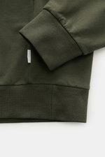Nahaufnahme eines dunkelgrünen 04651/ A trip in a bag Sweat-Troyer 'IF' mit elastischer Rippbündchen, kleinem Weblabel, weichem Griff, garment dyed, Regular Fit, Troyer-Kragen mit verdecktem Zipper, softer Innenseite, aus reiner Baumwolle, fotografiert vo