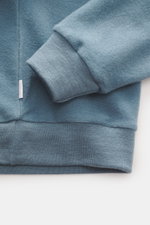 Nahaufnahme des rauchblauen 04651/ A trip in a bag Rundhals-Sweatshirts mit weichem Jersey aus Wolle und Baumwolle, elastischem Bündchen, Slim Fit und inside-Out Design, fotografiert von schräg oben.