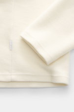 Nahaufnahme des Ärmels und unteren Bereichs von 04651/ A trip in a bag Troyer 'CW Zip Polo' creme, Regular Fit, weicher Griff, Mix aus Wolle und Baumwolle, klassischer Troyer-Kragen, innenliegende Brusttasche, kleines Weblabel in der Seitennaht.