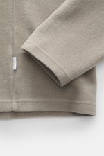 Nahaufnahme von Ärmel und Saum des 04651/ A trip in a bag Troyer 'CW Zip Polo' taupe, aus weichem Woll-Baumwoll-Mix, Regular Fit, mit klassischem Troyer-Kragen, innenliegender Brusttasche und kleinem Weblabel in der Seitennaht, frontal fotografiert.