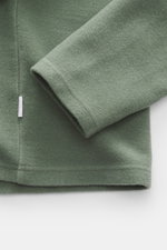 Nahaufnahme des Ärmels von 04651/ A trip in a bag Troyer 'CW Zip Polo' salbei in Regular Fit, weicher Griff, Mix aus Wolle und Baumwolle, klassischer Troyer-Kragen, innenliegende Brusttasche, kleines Weblabel in der Seitennaht, fotografiert von oben.
