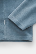 Nahaufnahme des rauchblauen 04651/ A trip in a bag Troyer 'CW Zip Polo' aus Wolle-Baumwoll-Mix, weicher Griff, Regular Fit, klassischem Troyer-Kragen, innenliegender Brusttasche und kleinem Weblabel in der Seitennaht, fotografiert von der Ärmel- und Saum-