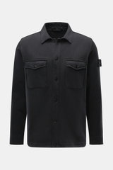 Front view of the Stone Island Sweatjacke 'Ghost' schwarz, a black cotton sweat jacket with a fold-over collar, button closure, chest pockets, and the brand's compass badge on the sleeve.

<p>Zeitloses Layering-Piece: Die Sweatjacke aus der 'Ghost' Capsul