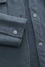 Close-up front view of Stone Island Sweatjacke 'Ghost' graublau showing grey-blue cotton fabric, snap buttons with logo, folded cuff, and textured knit. <p>Zeitloses Layering-Piece: Die Sweatjacke aus der 'Ghost' Capsule Collection von STONE ISLAND überze