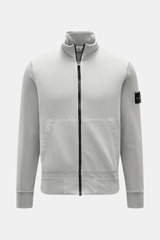 Stone Island Sweatjacke hellgrau, frontal fotografiert, aus softer Baumwolle, mit Reißverschluss, Stehkragen, Kängurutasche, Kompass-Badge.