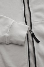 Stone Island Sweatjacke hellgrau, detailnah fotografiert von vorne, mit weichem Baumwollstoff, robustem Reißverschluss und Rippbündchen.