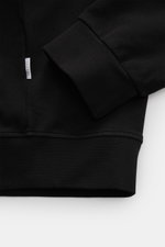 Schwarz fotografierte Detailansicht der 04651/ A trip in a bag Sweatjacke 'IF Track' schwarz mit elastischen Rippbündchen und Weblabel am Saum, super softer Baumwoll-Jersey.